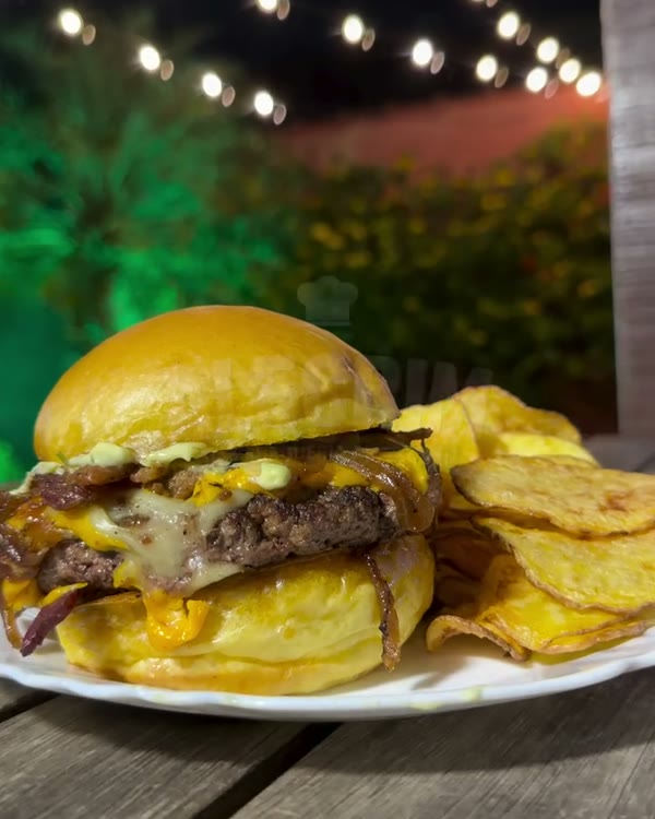 Hambúrguer com queijo e batata chips no jardim iluminado